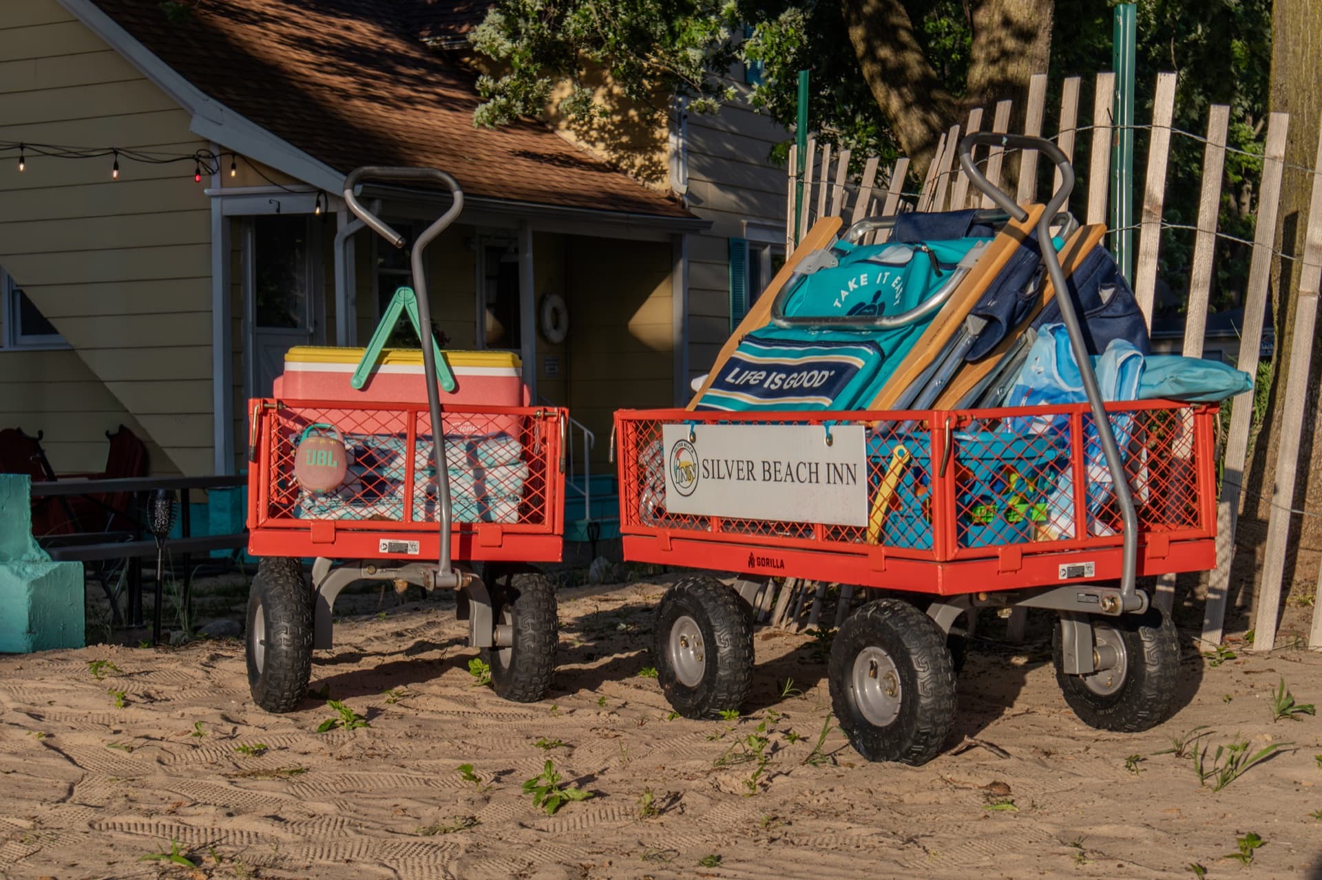 Two red beach wagons labeled Silver Beach Inn, loaded with chairs and a cooler, staged in the sand at golden hour